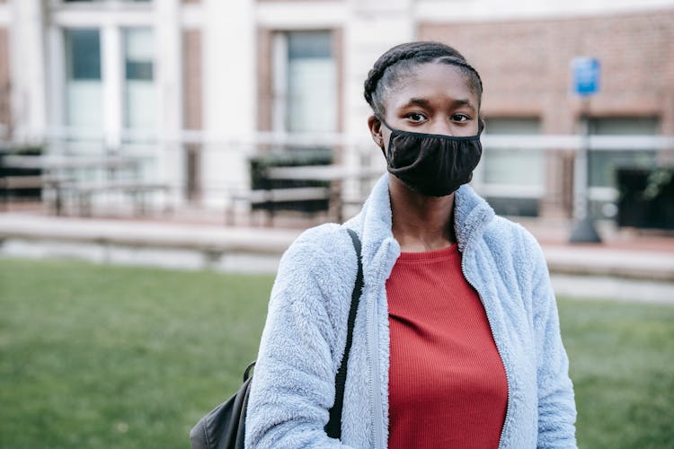 Unrecognizable Black Woman In Mask Against Urban Lawn