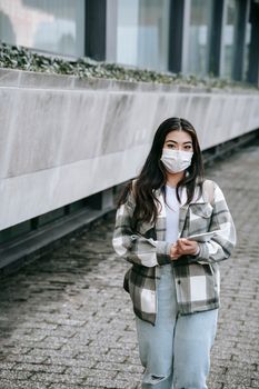 一名年轻女子穿着休闲装、戴着口罩，站在城市环境中