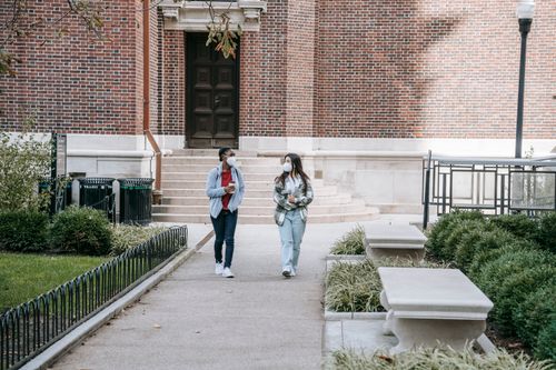 Free Full body of young multiethnic female students in casual clothes and medical masks walking in campus park after lessons Stock Photo