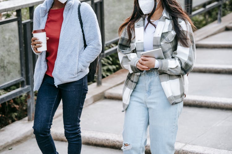 Anonymous Female Teens Walking In Park With Takeaway Coffee And Tablet In Hands