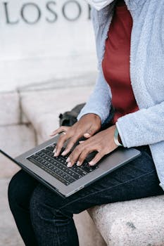 Casually dressed woman using laptop outdoors while maintaining social distance.