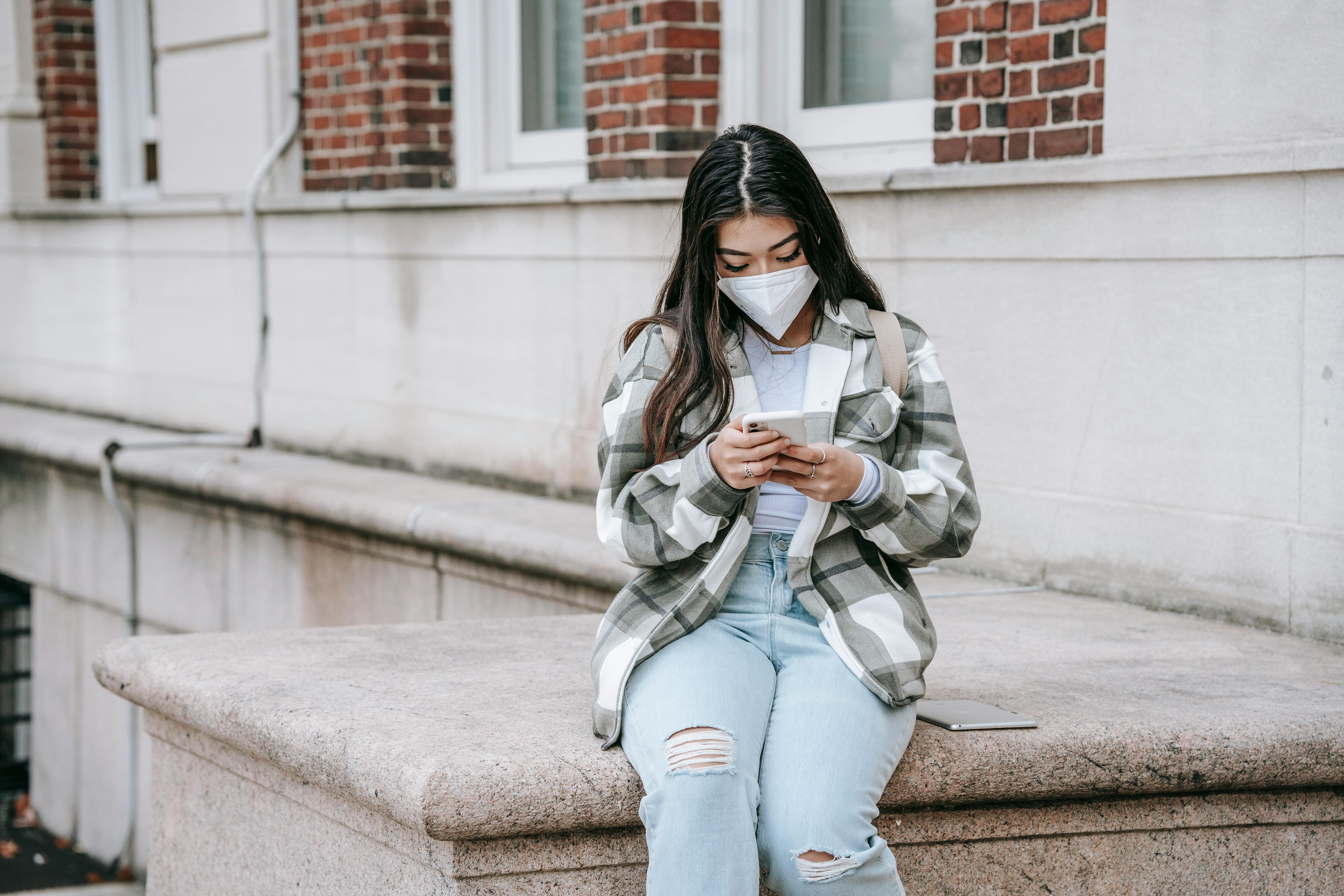 serious young ethnic lady messaging on smartphone near university building