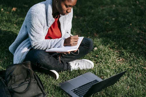 Macbook Pro를 사용하여 녹색 잔디밭에 앉아 회색 스웨터와 검은 색 바지를 입은 남자