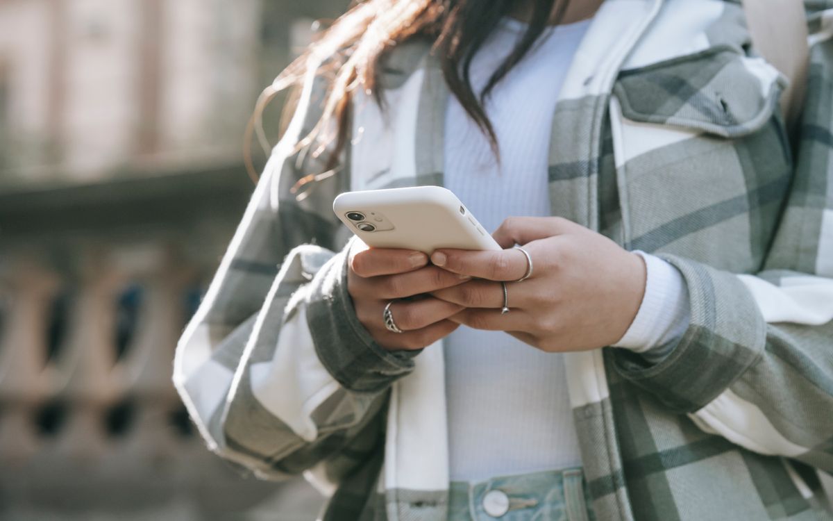 Crop faceless young woman in casual outfit text messaging on phone in city street in daytime