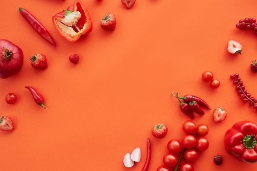 A colorful array of red fruits and vegetables on an orange background, featuring peppers, strawberries, and tomatoes.