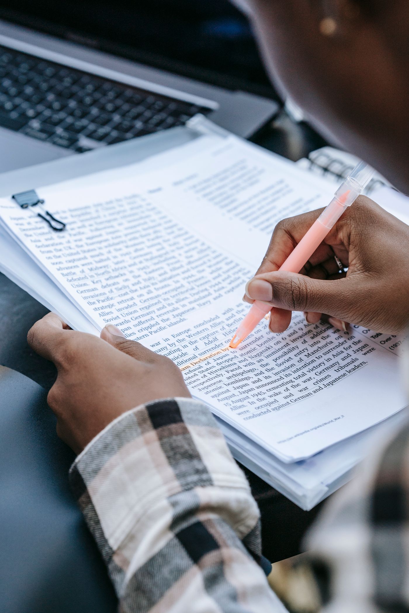 Personne relisant et surlignant un document à côté d’un ordinateur portable
