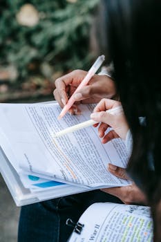 Close-up of students highlighting notes in textbooks, studying for exams outdoors.