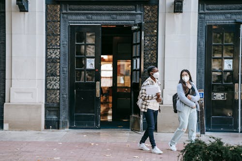 Free Young diverse women in masks walking together on city street Stock Photo