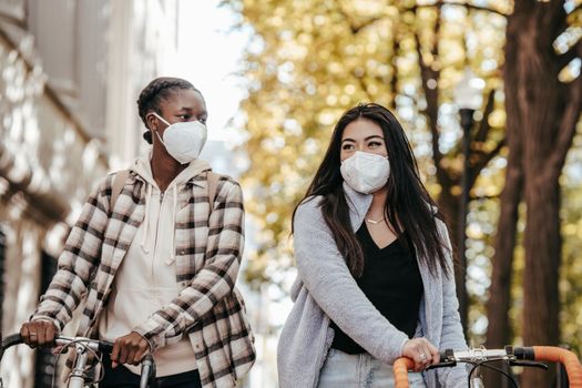 两名妇女戴着口罩，骑着自行车，在户外享受阳光明媚的一天，这象征着友谊与安全