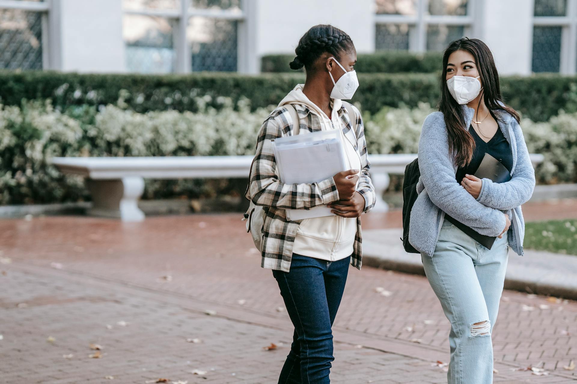 Two young women wearing masks walking and talking outdoors, embracing the new normal on campus.