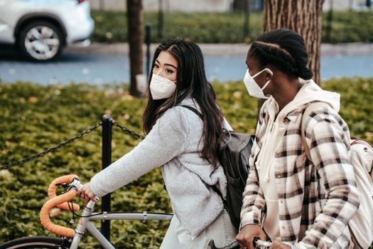 大流行期间，多种族女性朋友在公园里边骑自行车边散步、相互交流的侧面图