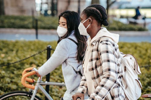 Diverse girlfriends wearing masks walking with bicycles