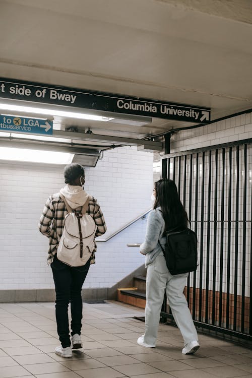 Free Back view full length of unrecognizable multiracial students in masks with backpacks walking in subway station Stock Photo