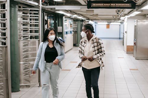 Multiracial women in protective masks walking together in hallway of subway and looking at each other