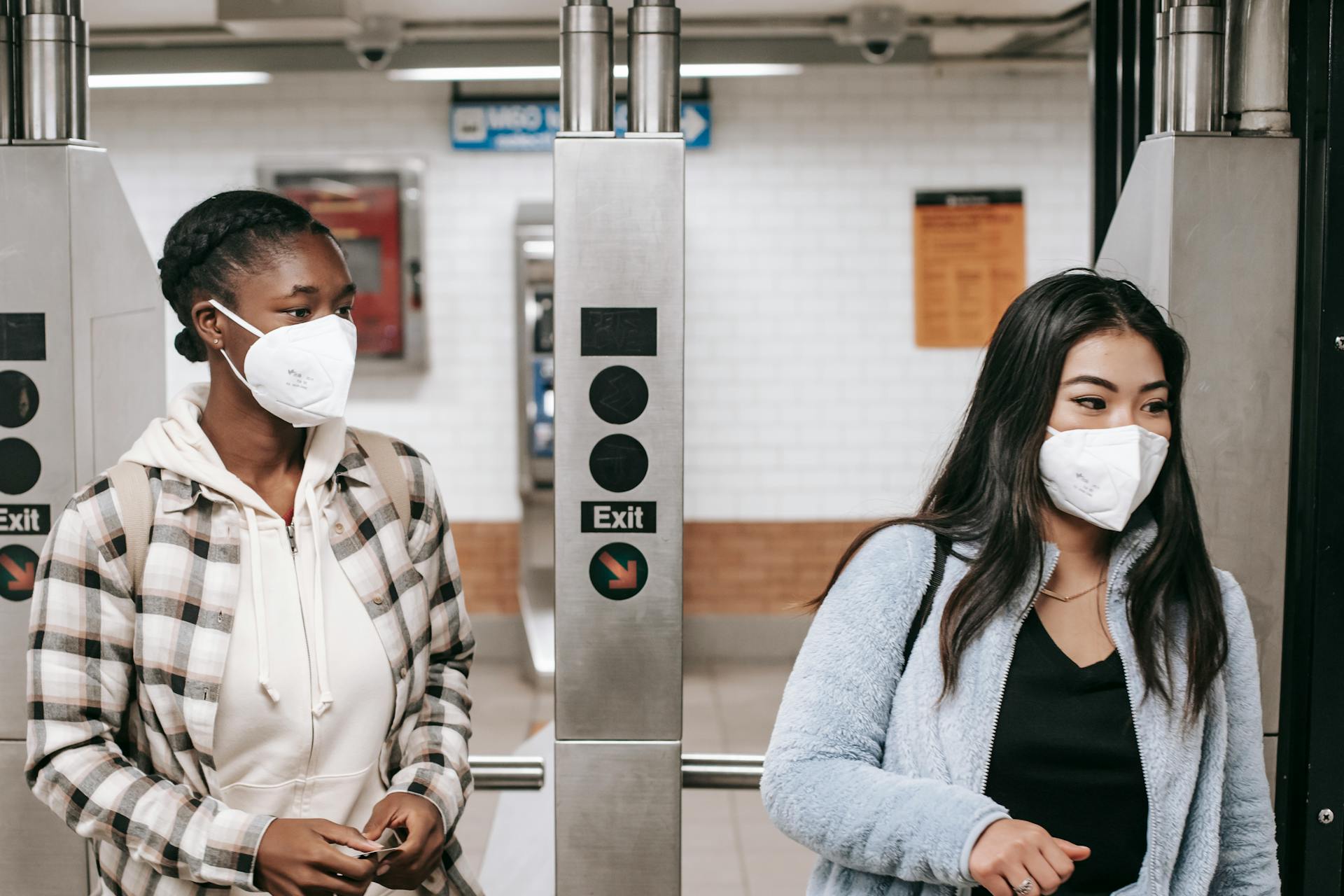 Multiethnic girlfriends in casual wear and protective masks entering metro station during coronavirus epidemic