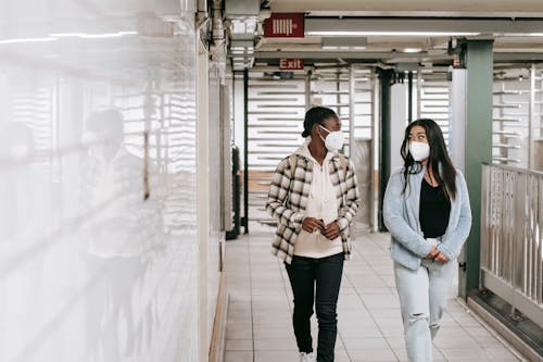 Multiracial women in protective masks walking in passage of underground during coronavirus epidemic and looking at each other
