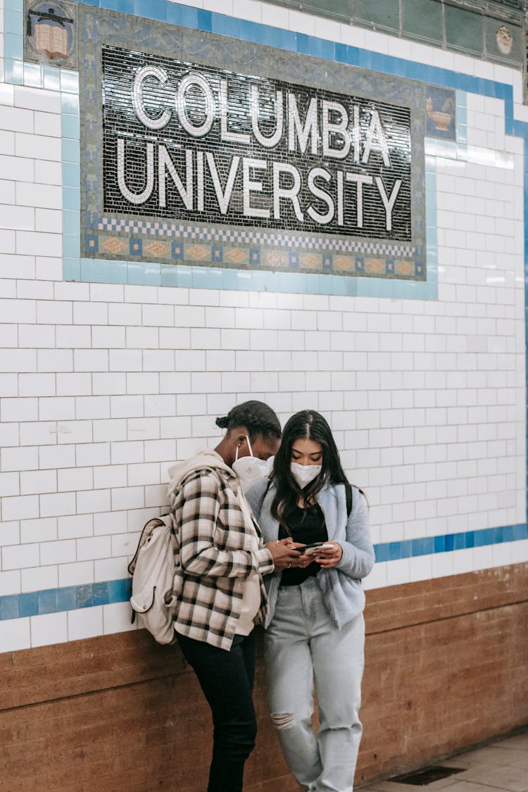 Unrecognizable Diverse Girlfriends Chatting On Smartphones In Underground