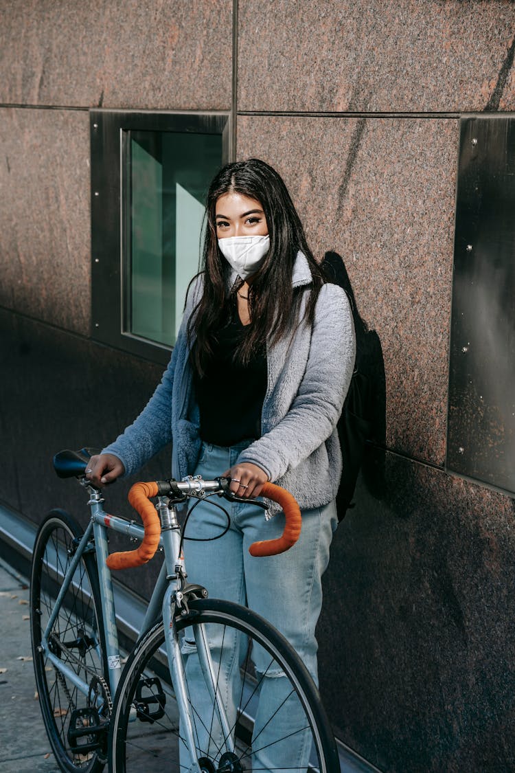 Unrecognizable Asian Woman In Mask With Bike In Town