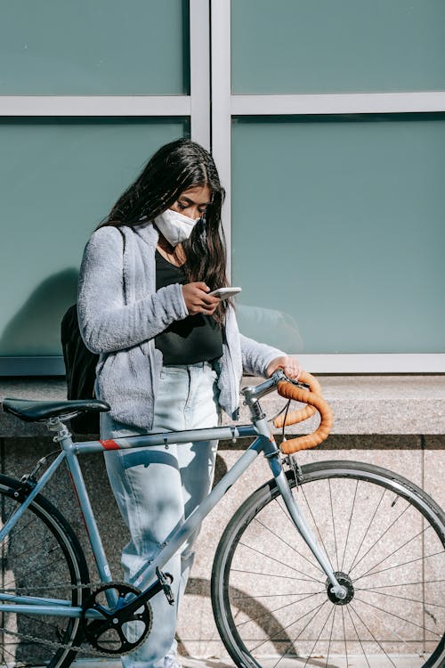 Wanita Dengan Mantel Abu Abu Dan Jeans Denim Biru Duduk Di Sepeda Biru