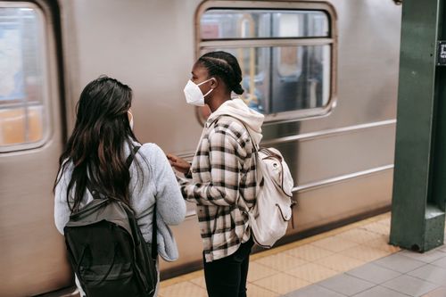 Free Back view of unrecognizable multiracial girlfriends in respiratory masks with backpacks against public transport in underground Stock Photo