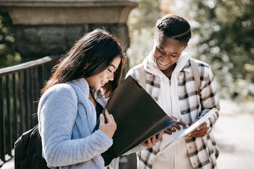 Cheerful multiracial students watching folders while studying on street