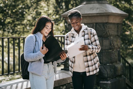Two friends studying together outdoors in a park, enjoying the sunlight and friendly conversation.
