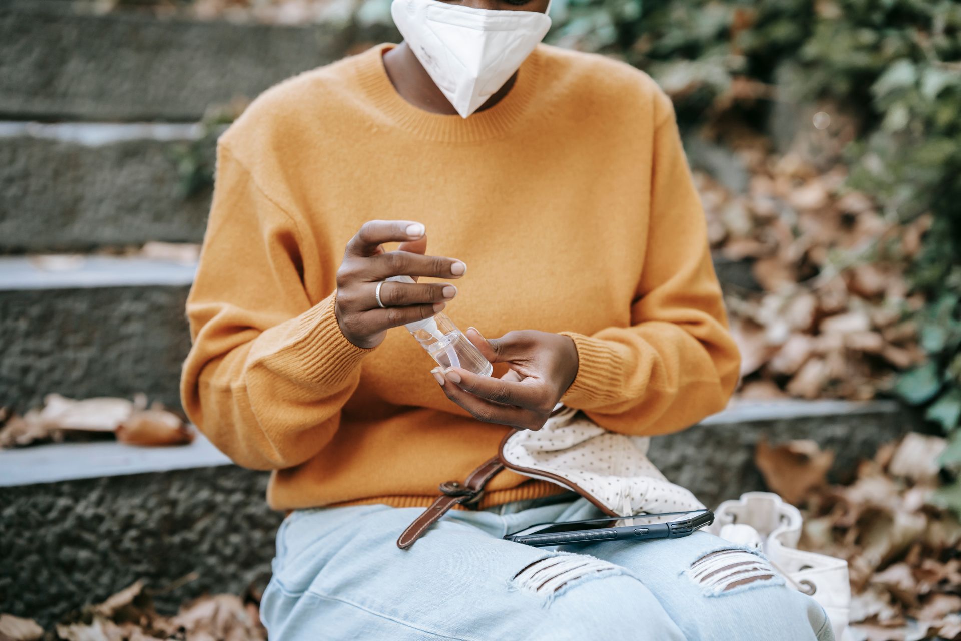 Crop unrecognizable black woman in mask using sanitizer in park