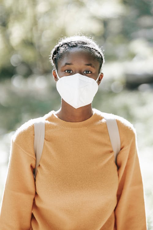 Calm black woman in mask standing in sunny park