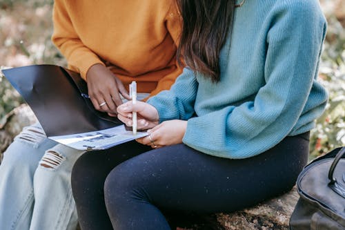 Crop faceless multiethnic schoolgirls doing homework together in park