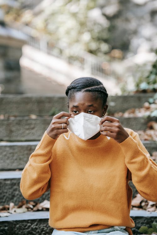 Young black woman putting on protective mask in park