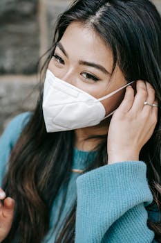 Asian woman adjusting face mask with a smile on a sunny outdoor day.