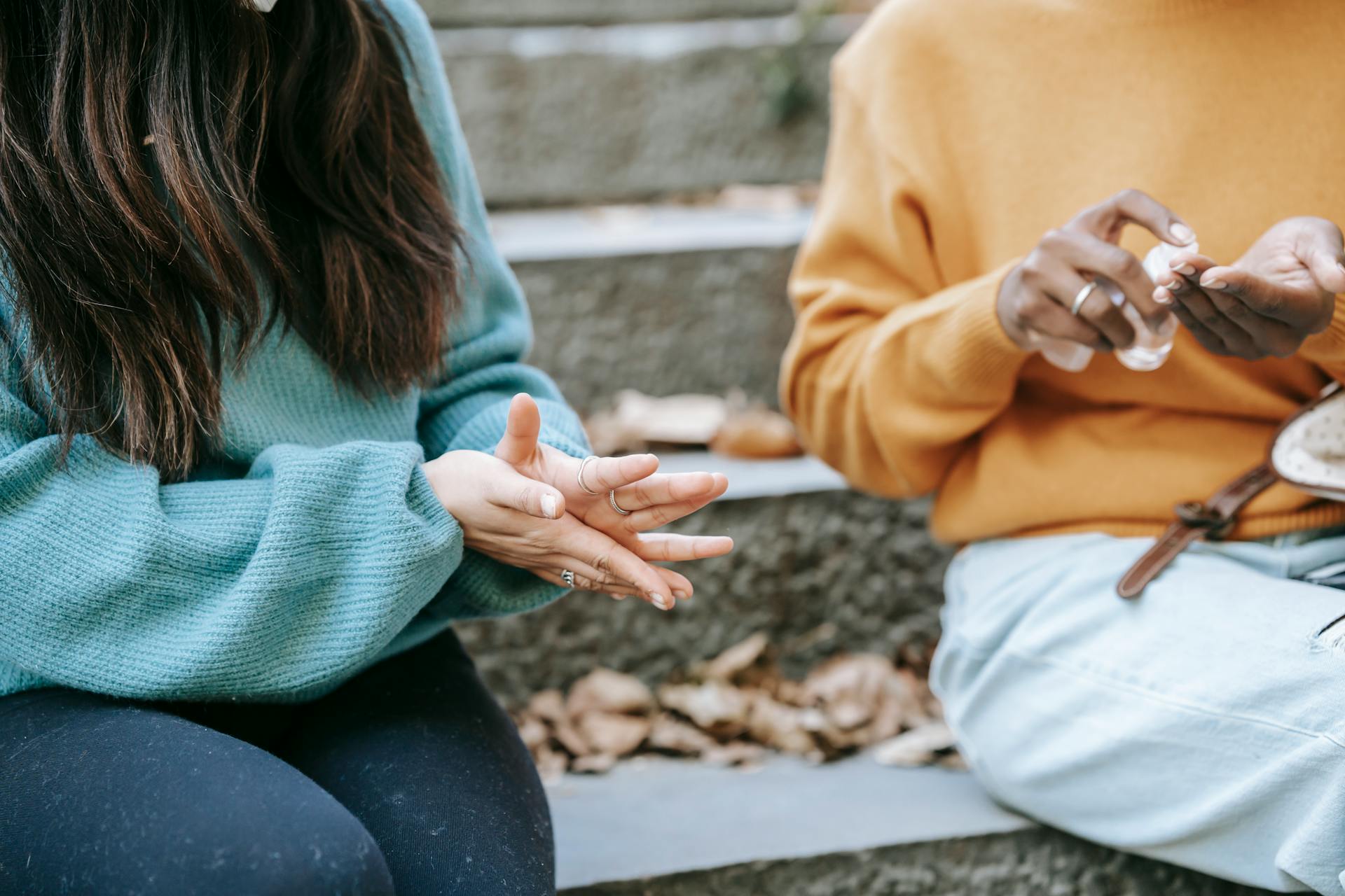 Two friends applying hand sanitizer while sitting outdoors in a park during fall.