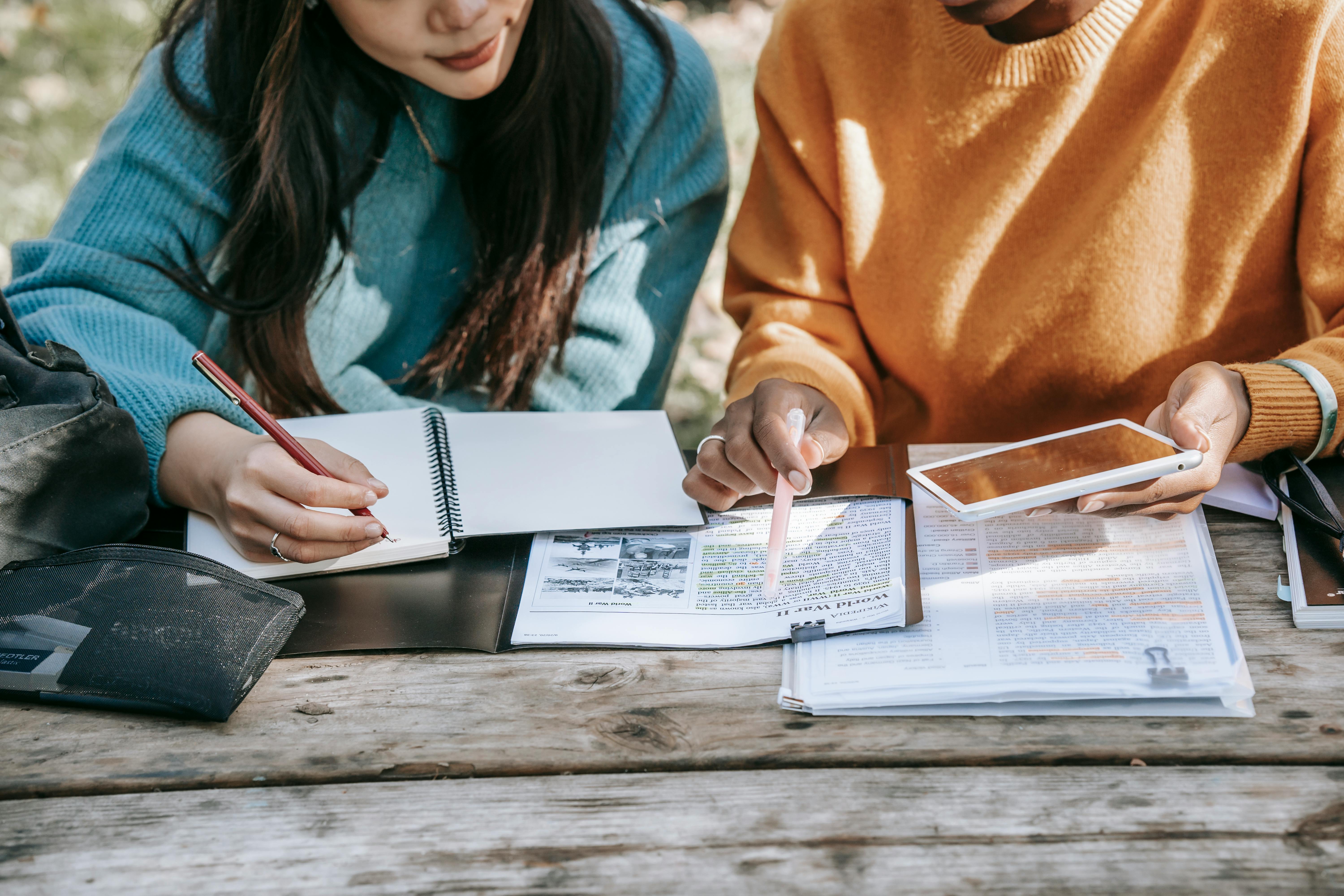 crop diverse female students fulfilling homework together in park