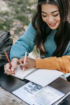 From above of happy crop multiethnic students taking notes in copybook while reading information on paper at table