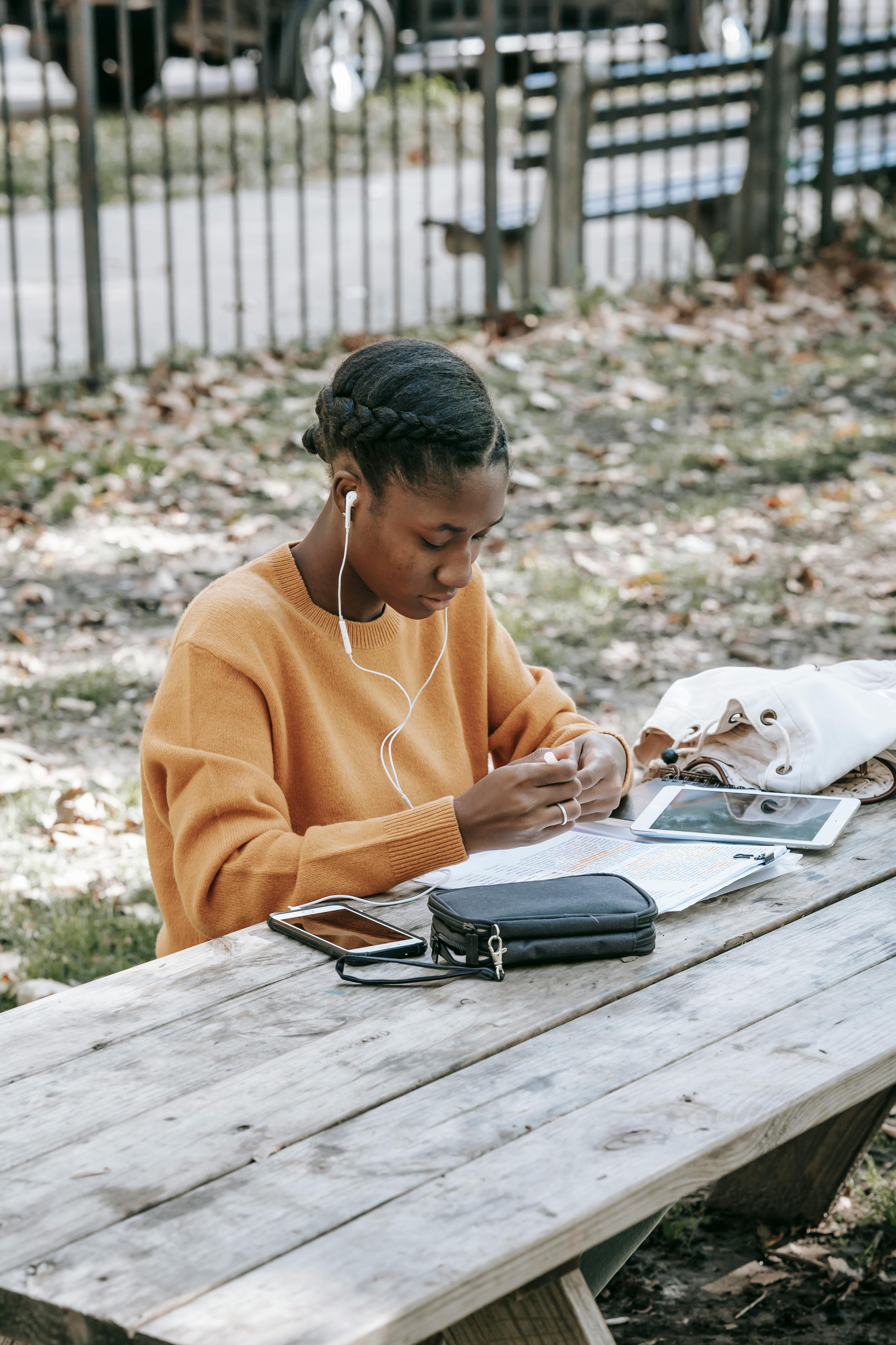 focused young black woman with earphones studying information in notebook