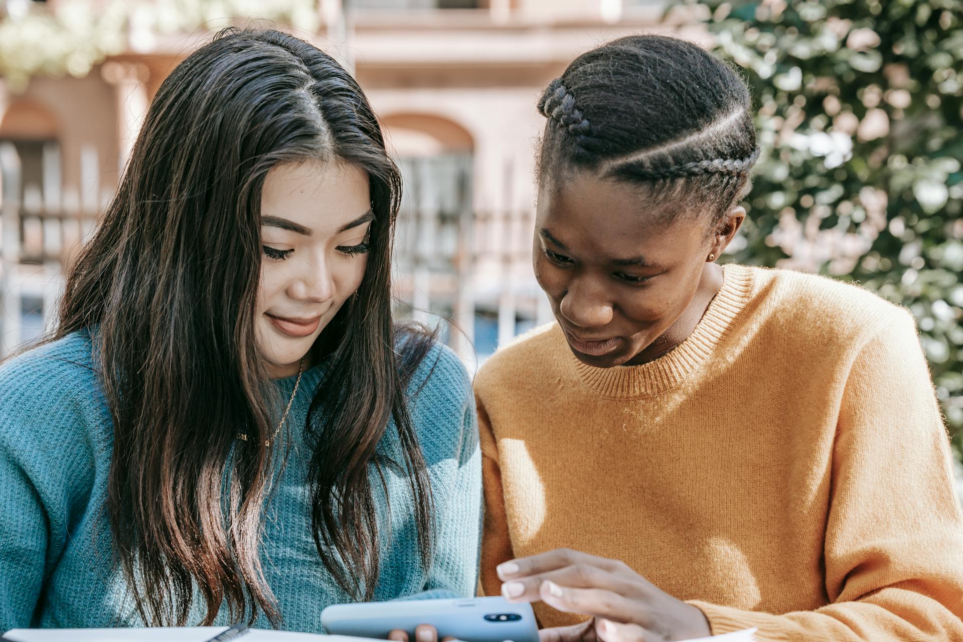 Happy multiethnic women watching video online with smartphone on street