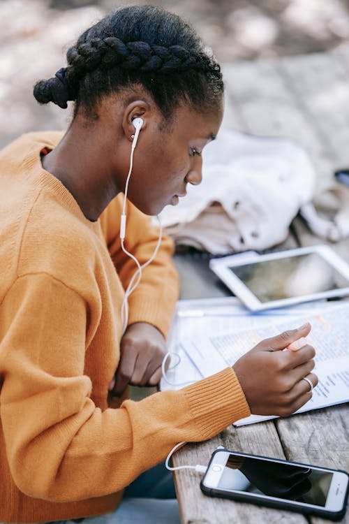 Young black woman in earphones studying while using smartphone