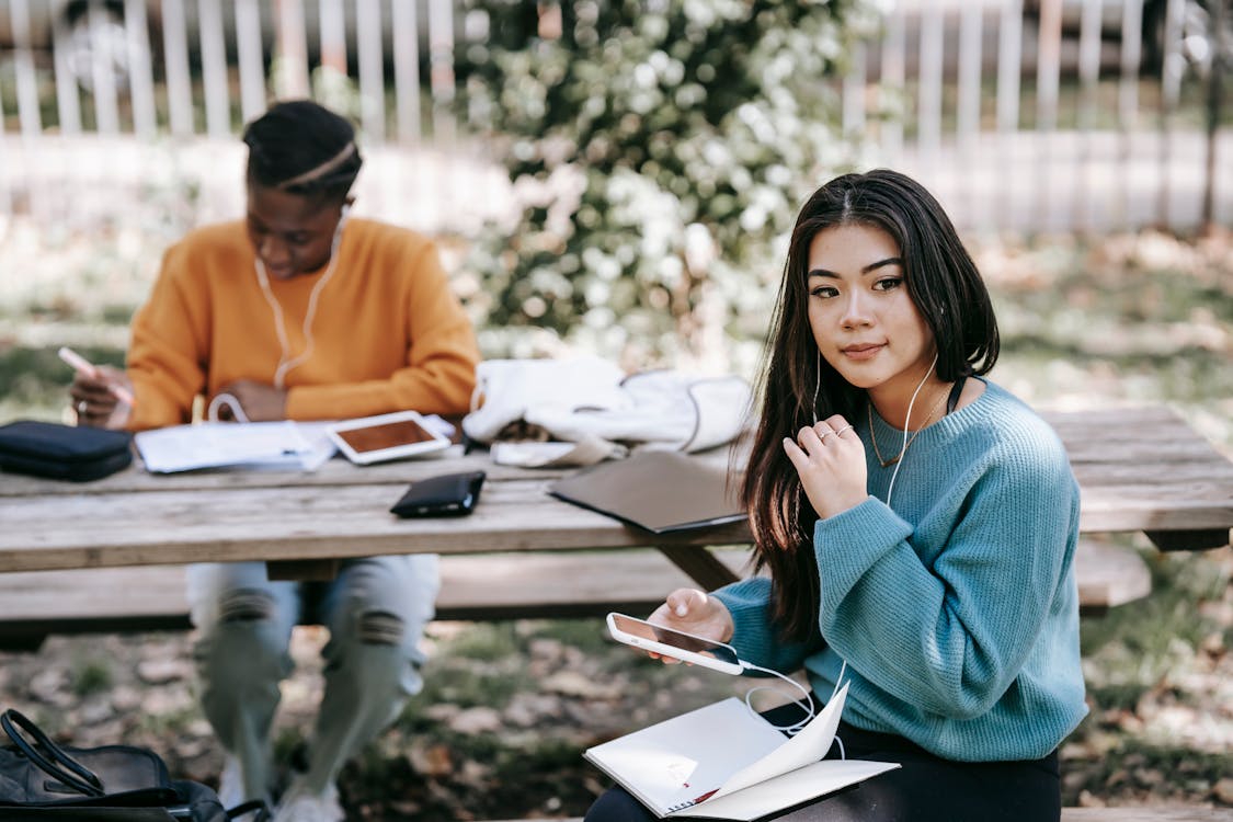 Free Pensive young multiethnic students working together with notebooks at table on blurred background of street Stock Photo