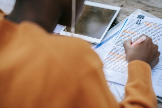 From above of crop anonymous African American person outlining text at table with tablet with black screen