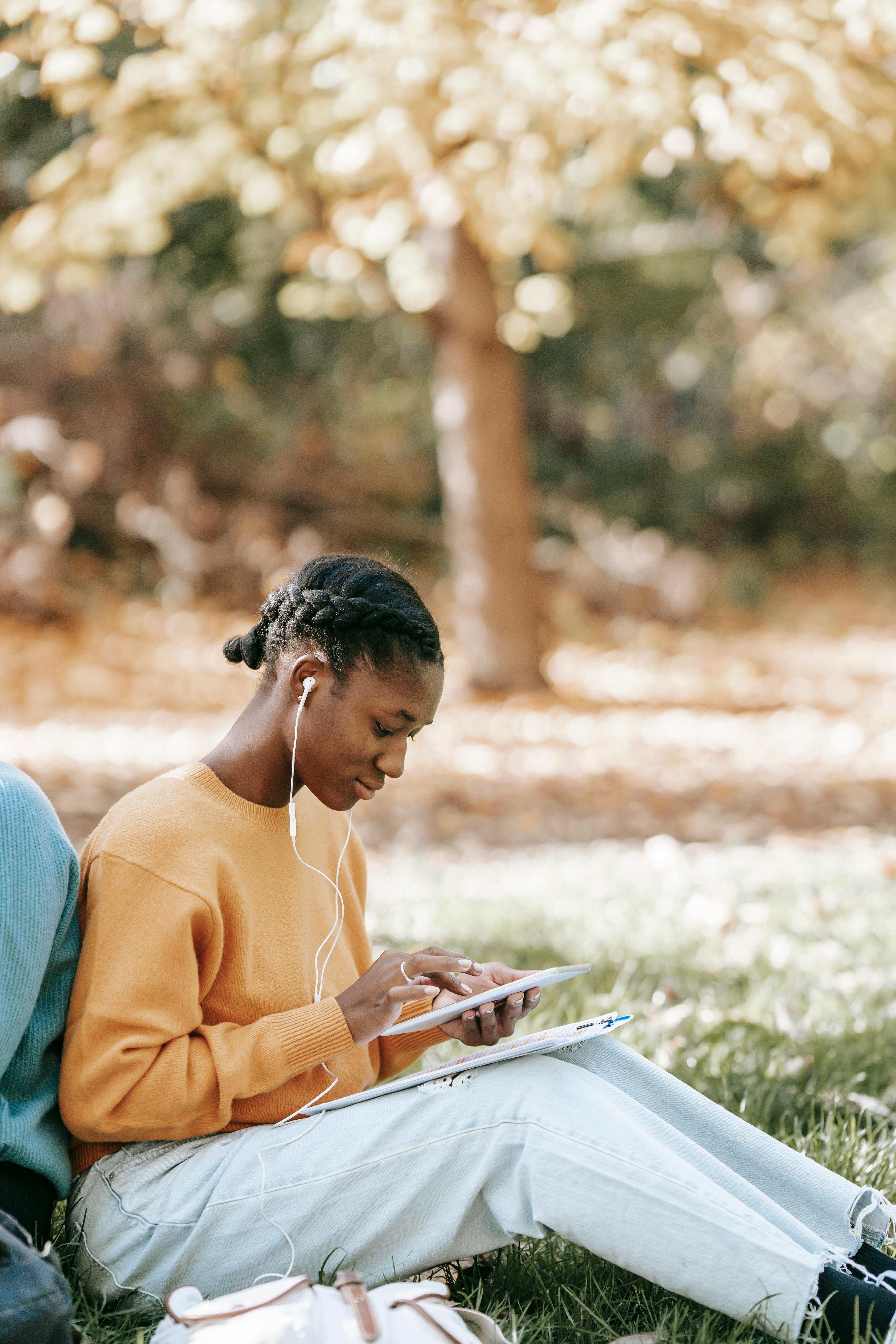 black woman in earphones surfing tablet in park