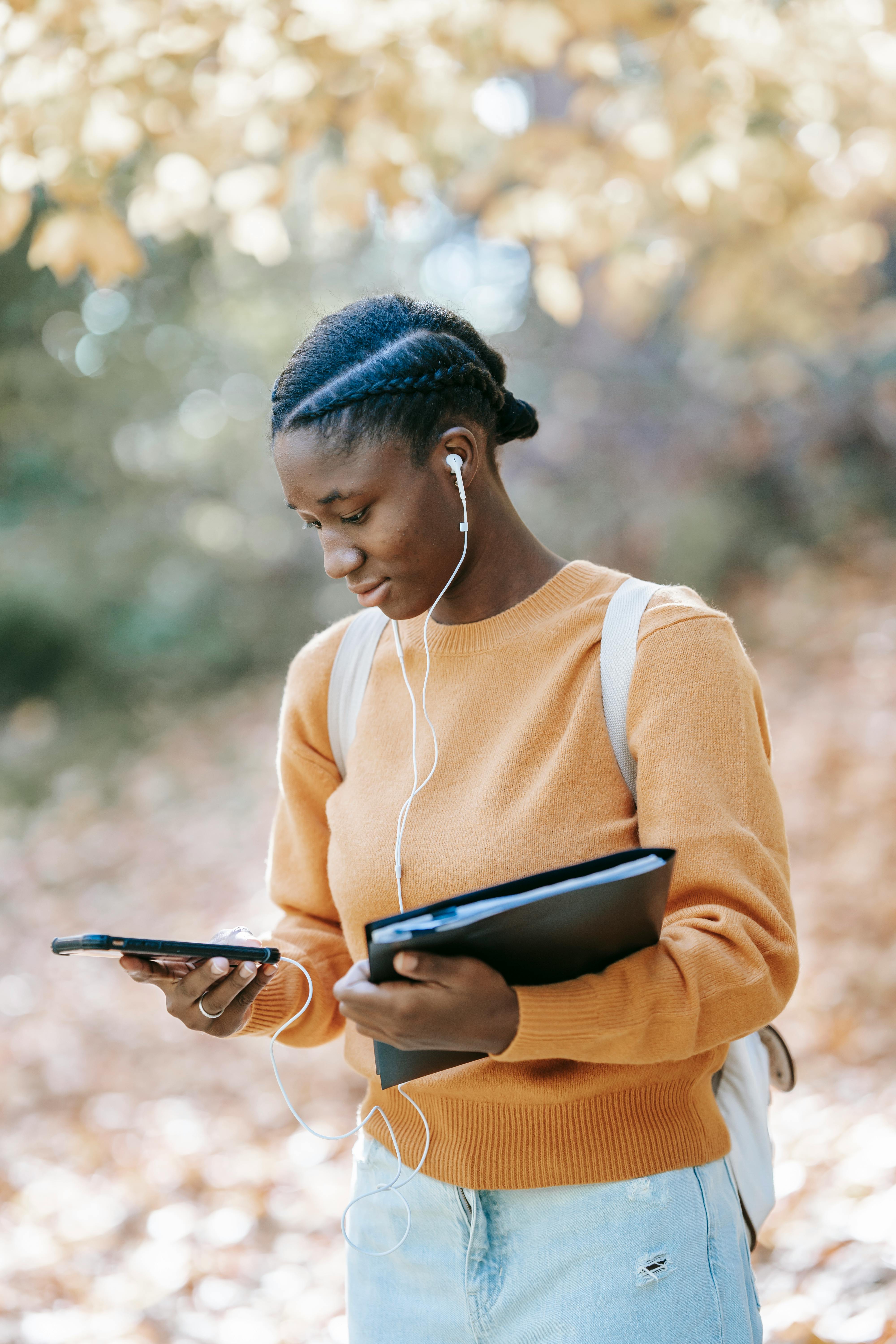 young black woman in earphones with folder checking smartphone