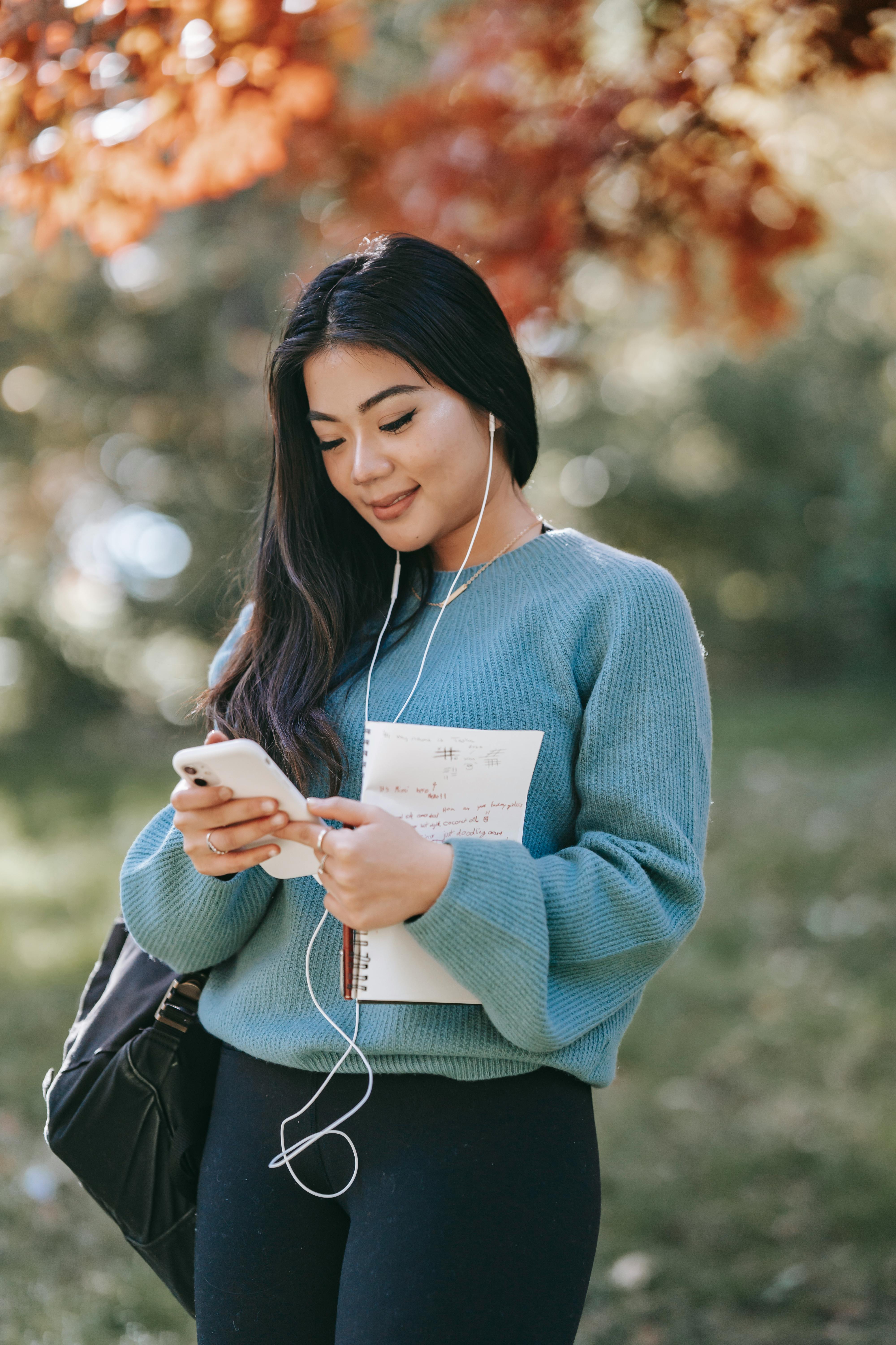 young cheerful woman listening to audio book using smartphone in park