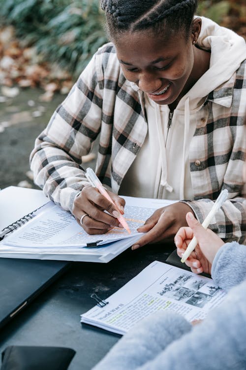 Crop multiracial students in casual clothes with pen taking notes while studying together