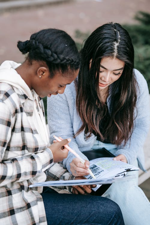 Focused multiracial students in casual clothes sitting on bench while preparing for exams together