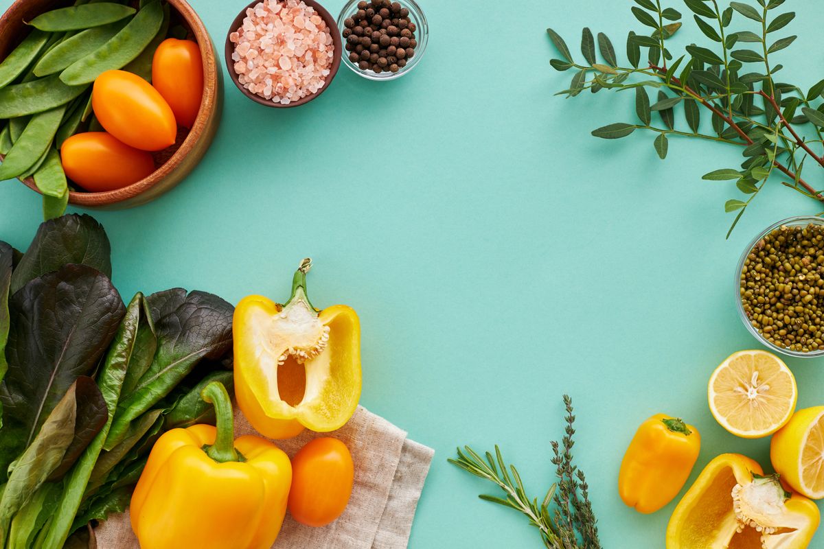 Fresh vegetables, herbs, and spices arranged in colourful bowls on a teal background, representing the variety of an Ayurvedic diet