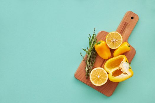 A vibrant display of yellow peppers, lemons, and herbs on a wooden board against a teal background.