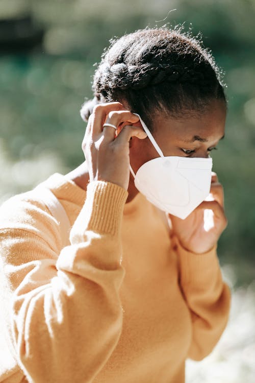 Young calm African American female student in casual wear and white protective mask with backpack walking in campus