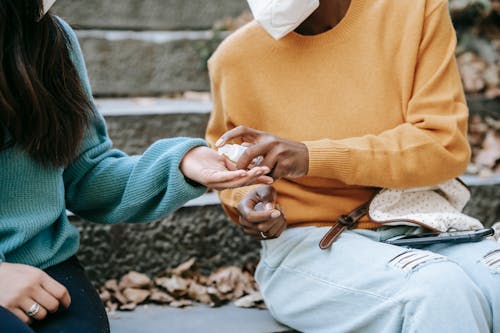 Crop diverse students on stairs treating hands with antiseptic