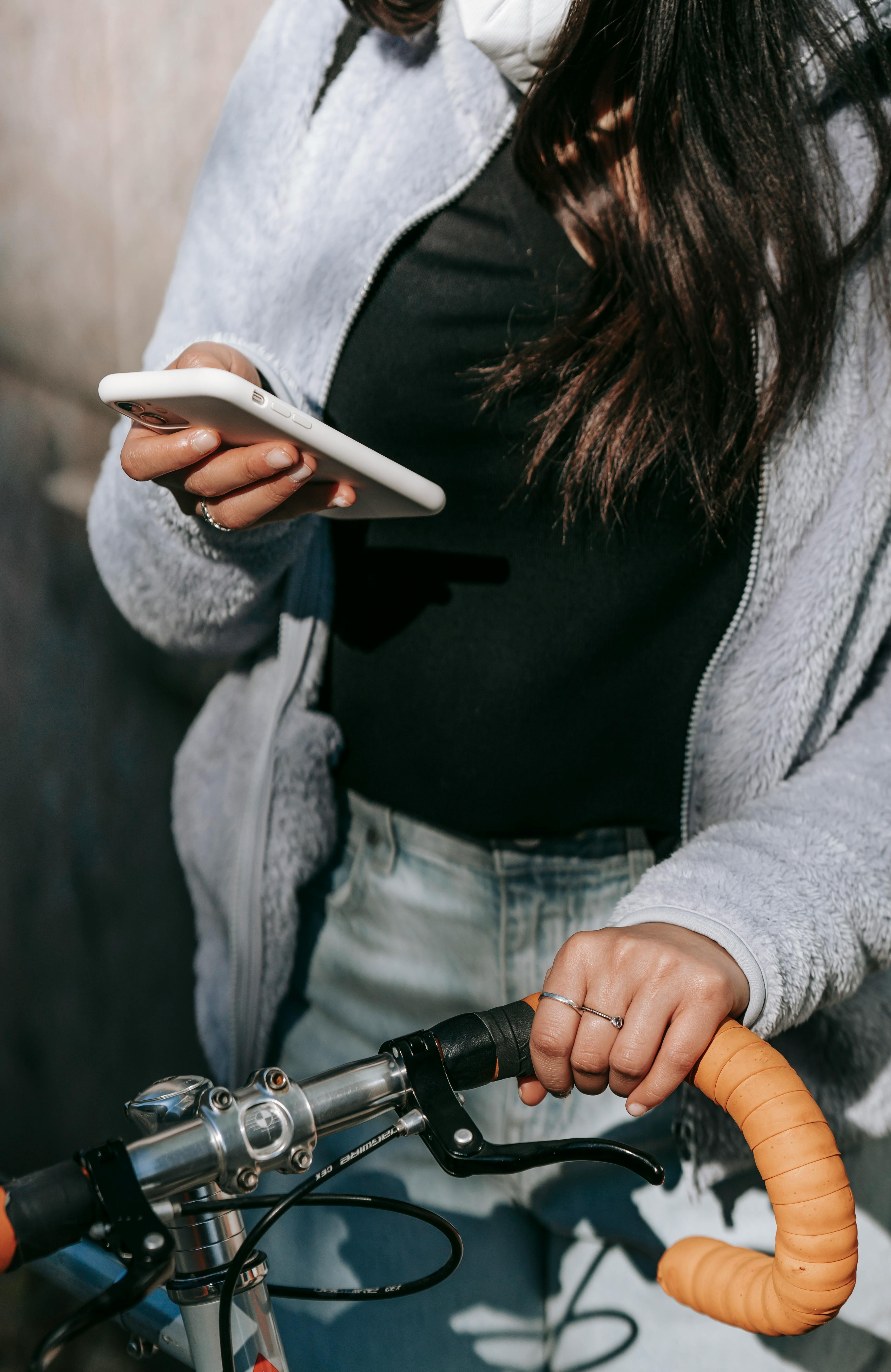 crop woman in mask text messaging on smartphone standing with bike