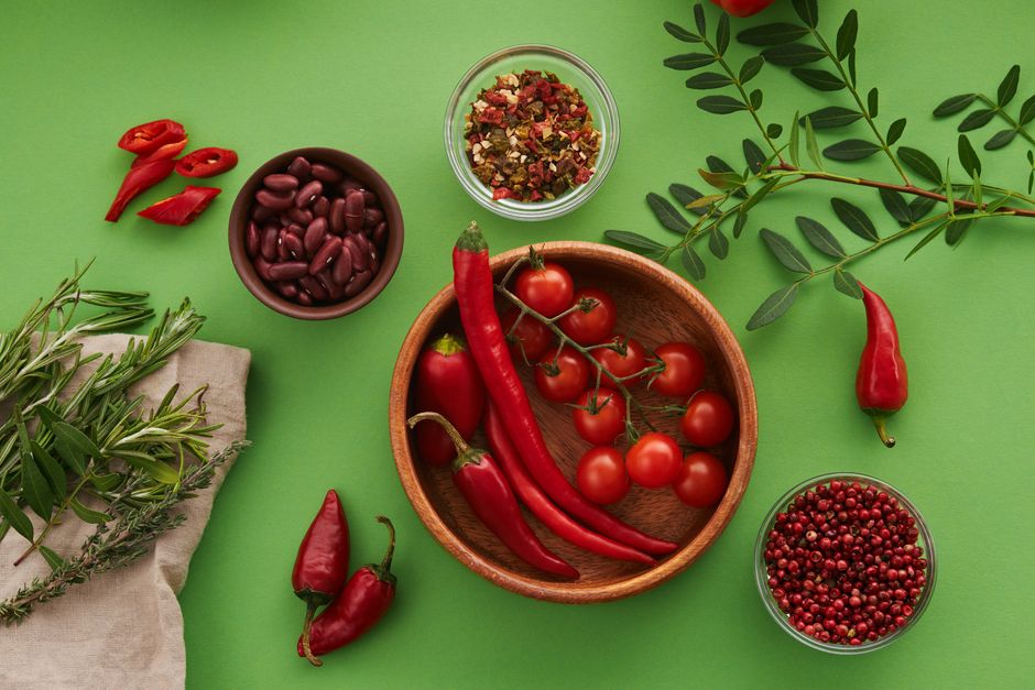 Top view of chilies, cherry tomatoes, beans, and herbs on green background. A colorful culinary arrangement.